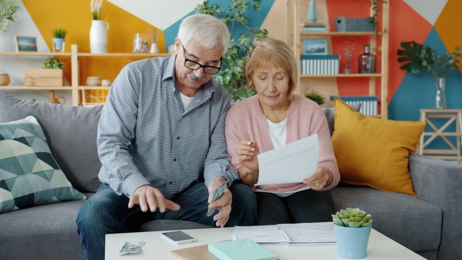 Elderly couple planning their budget, reviewing documents in a cozy living room.